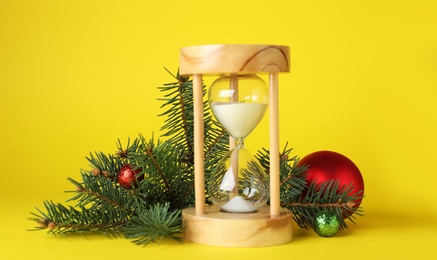 Photo of Hourglass and fir tree with decor on yellow background. Christmas countdown