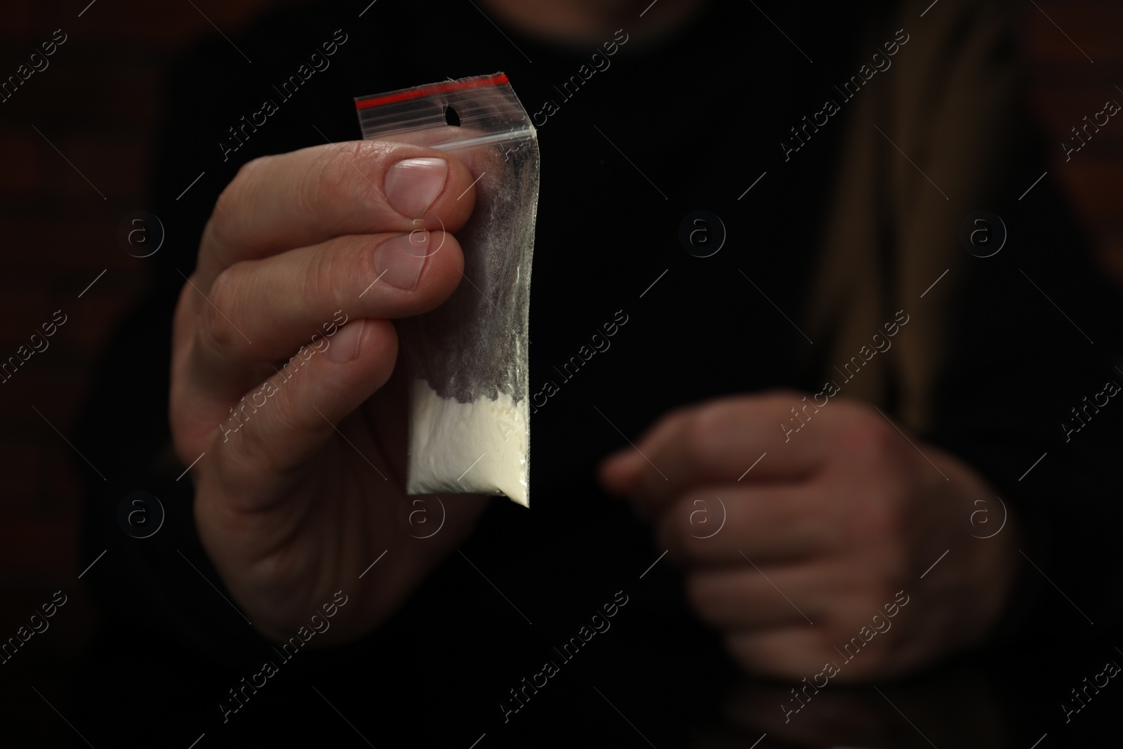 Photo of Drug addiction. Man with plastic bag of cocaine on dark background, closeup