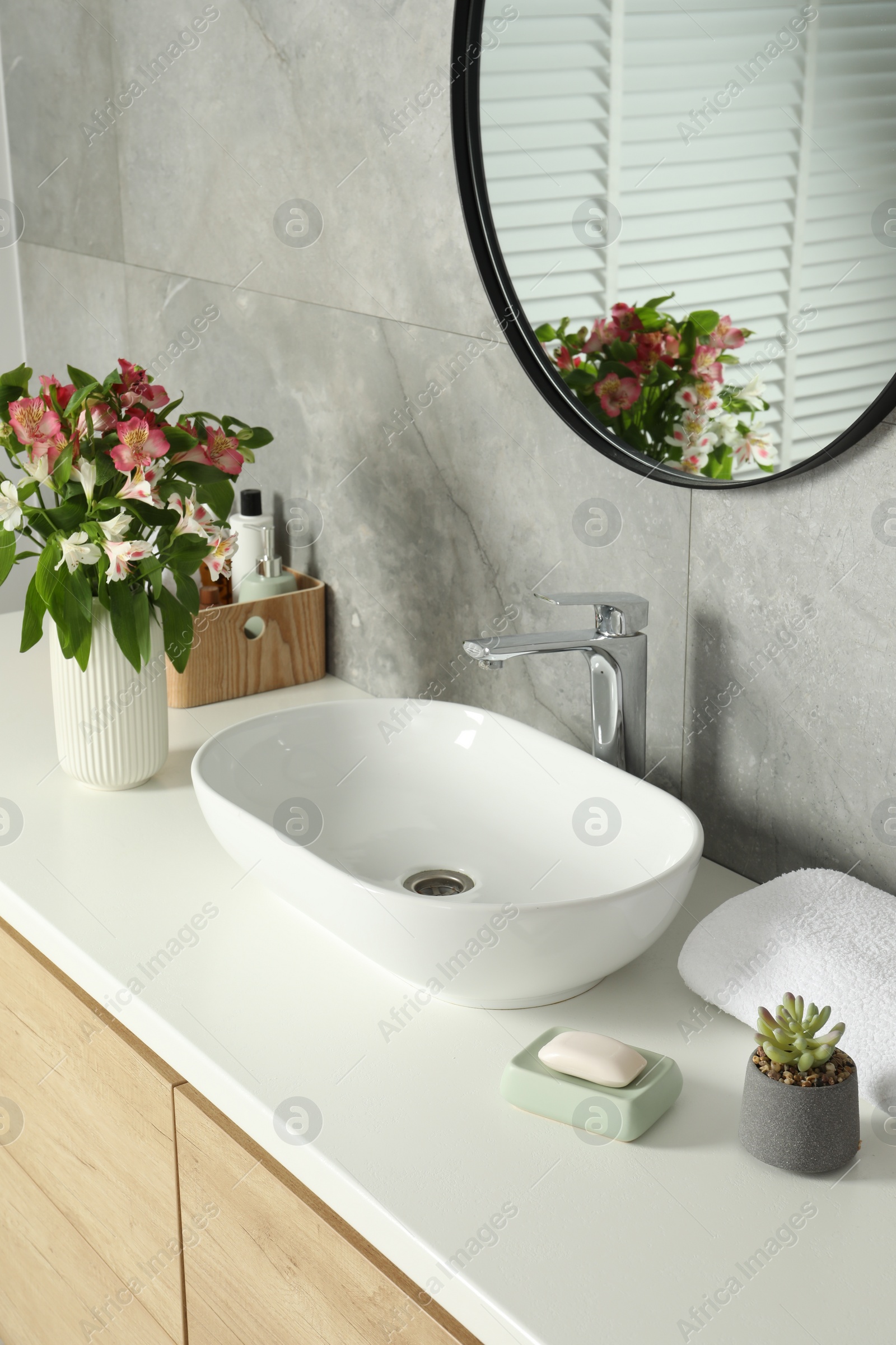 Photo of Vase with beautiful Alstroemeria flowers and toiletries near sink in bathroom