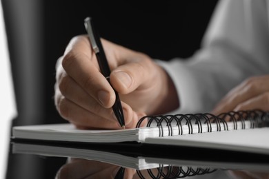 Photo of Man writing in notebook at black table, closeup