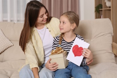 Young woman and her daughter with gifts on sofa at home