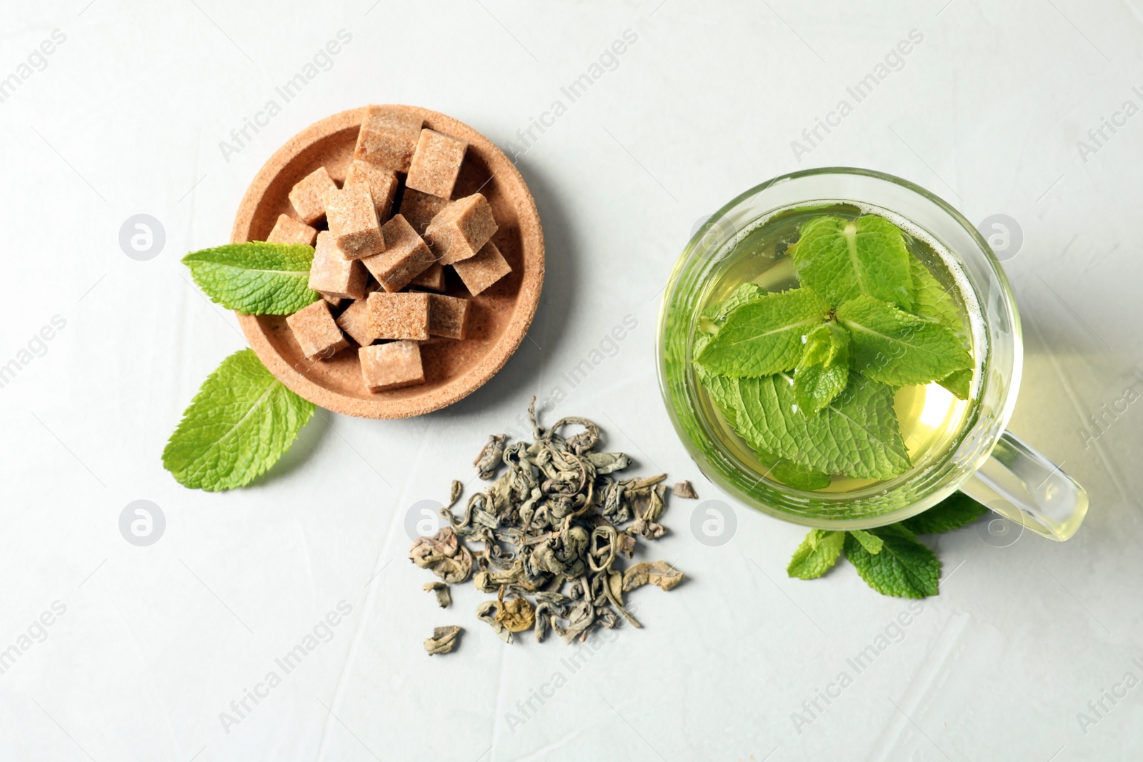 Photo of Cup with hot aromatic mint tea, dry leaves and sugar cubes on table, top view