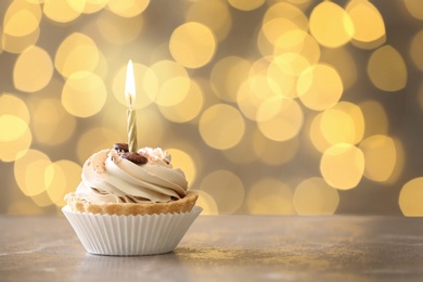 Tasty birthday cupcake with candle on table against blurred lights, space for text