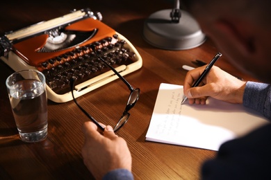 Man writing letter at wooden table indoors, closeup