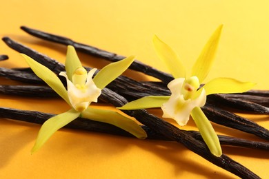 Photo of Vanilla pods and beautiful flowers on yellow background, closeup