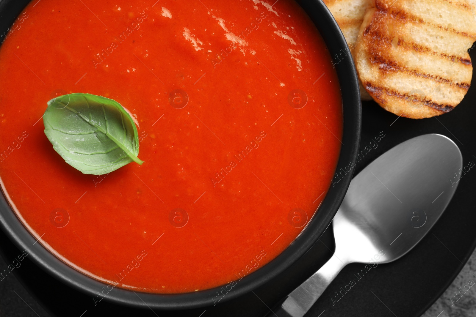 Photo of Delicious tomato cream soup in bowl and pieces of grilled bread served on table, top view