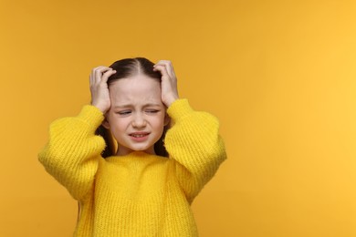 Little girl suffering from headache on yellow background