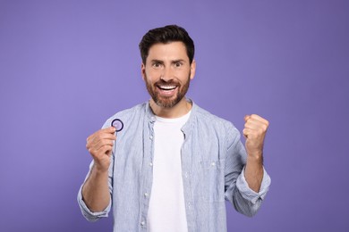 Photo of Emotional man holding condom on purple background. Safe sex