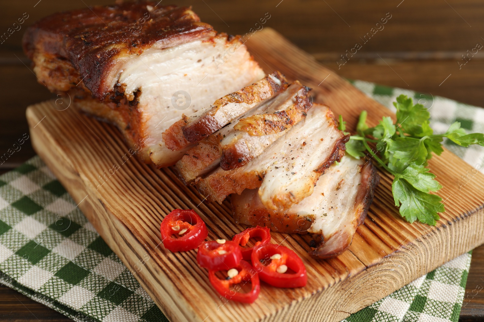 Photo of Pieces of baked pork belly served with chili pepper and parsley on wooden table, closeup