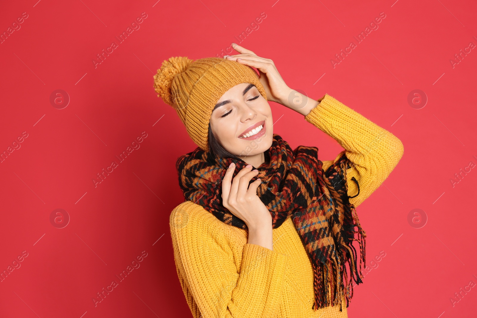 Photo of Young woman wearing warm sweater, scarf and hat on red background. Winter season