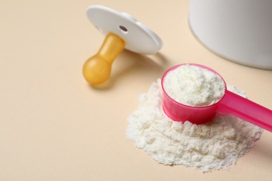 Photo of Powdered infant formula with scoop and pacifier on beige background, closeup. Baby milk