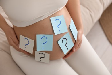 Photo of Pregnant woman with sticky notes on belly indoors, closeup. Choosing baby name