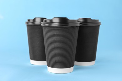 Photo of Paper cups with black lids on light blue background. Coffee to go