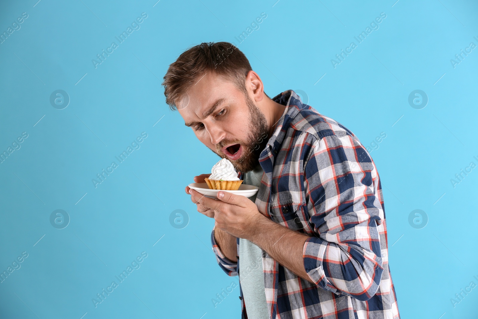 Photo of Greedy young man hiding cupcake on light blue background, space for text