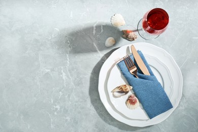 Elegant table setting with glass of red wine and seashells on grey marble background, flat lay. Space for text