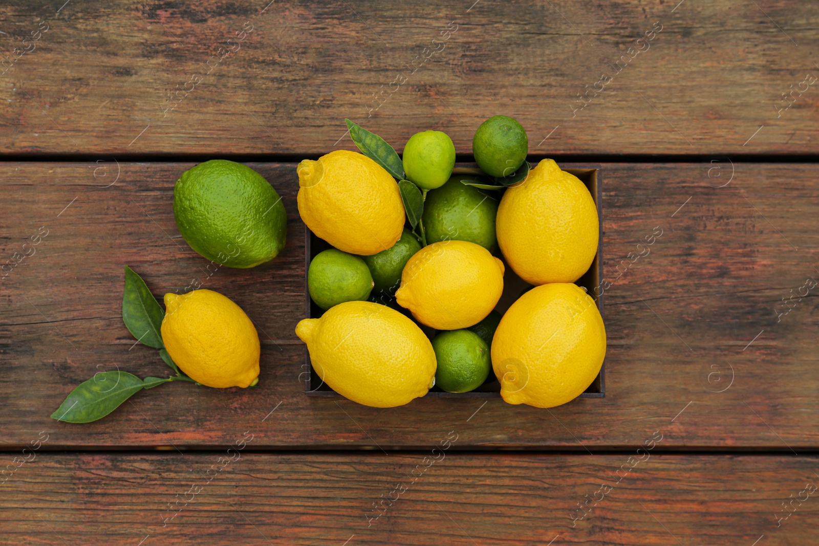 Photo of Many fresh lemons and limes with leaves on wooden table, flat lay