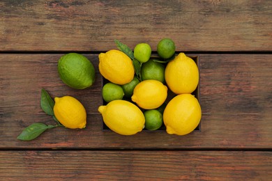 Photo of Many fresh lemons and limes with leaves on wooden table, flat lay