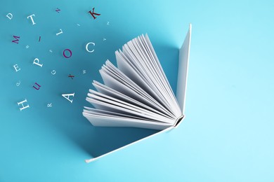 Image of Open book with letters flying out of it on light blue background, top view