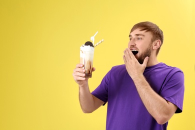 Young man with glass of delicious milk shake on color background