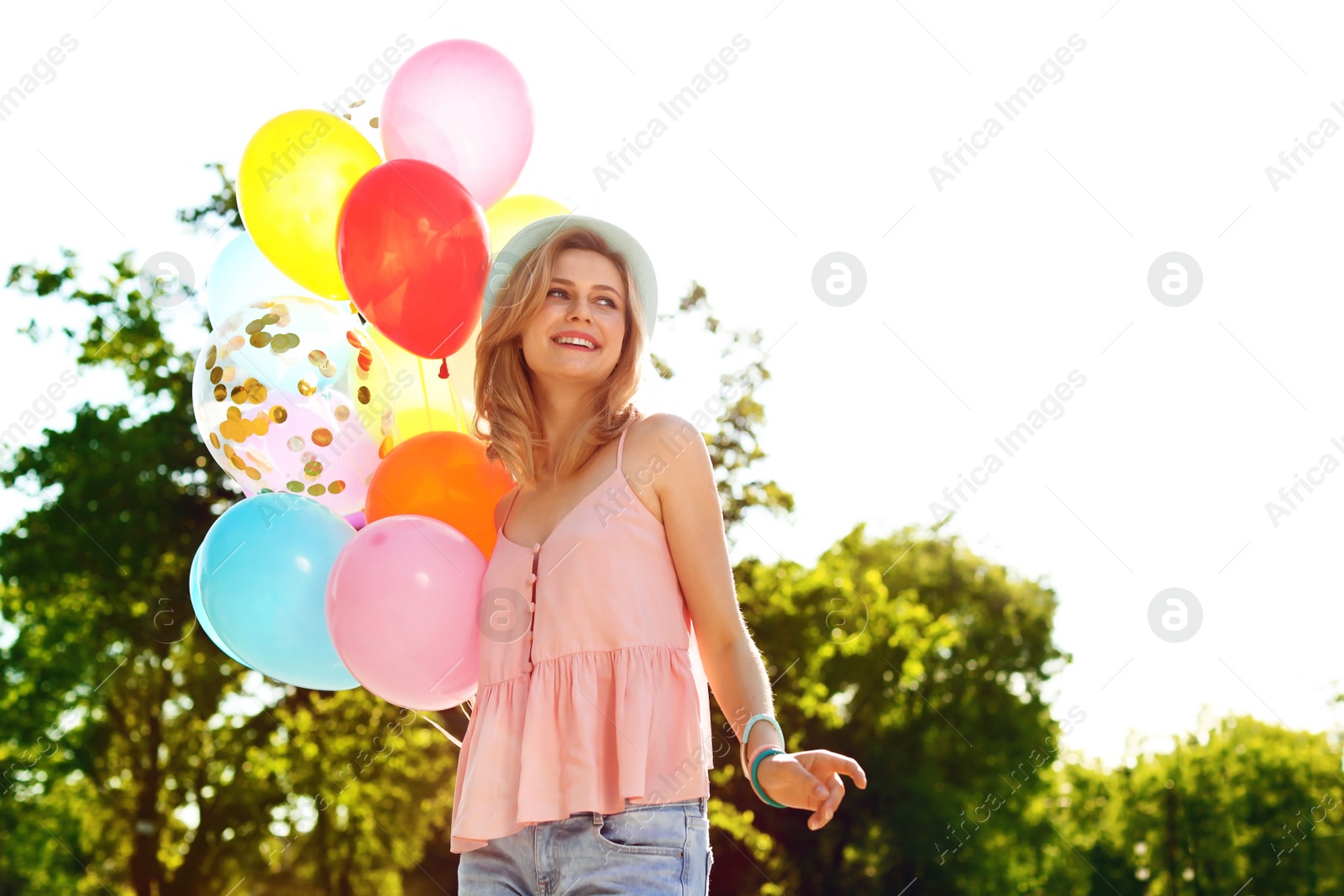 Photo of Young woman with colorful balloons outdoors on sunny day