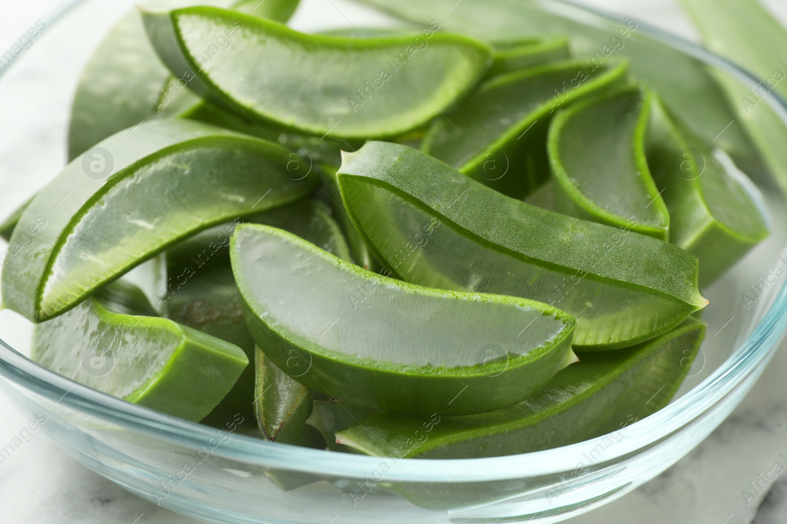 Photo of Fresh aloe vera slices in glass bowl on table, closeup