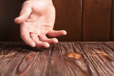 Photo of Man holding hand above wooden table, closeup. Space for text