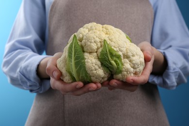 Woman holding fresh cauliflower against blue background, closeup