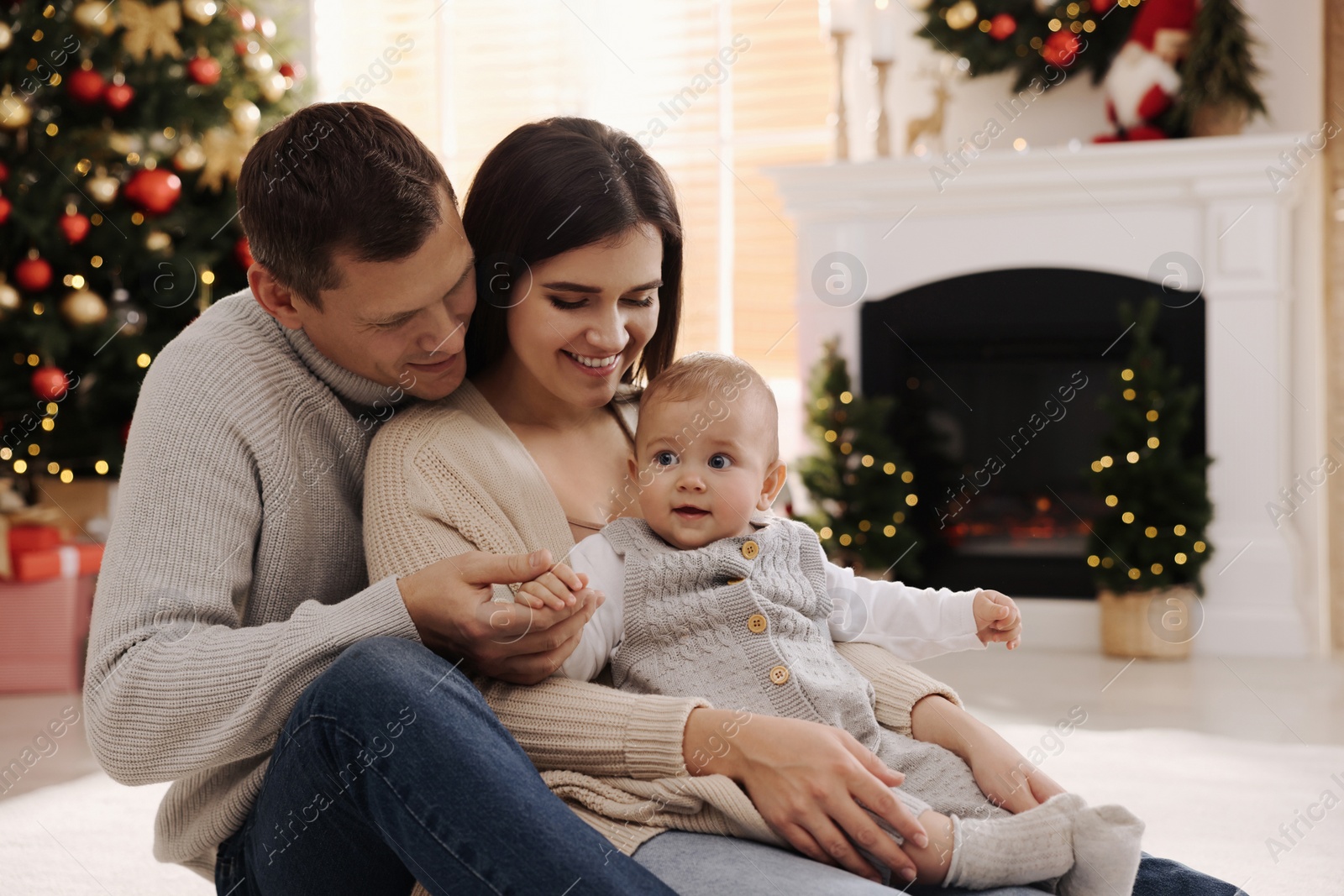 Photo of Happy family with cute baby on floor in room decorated for Christmas