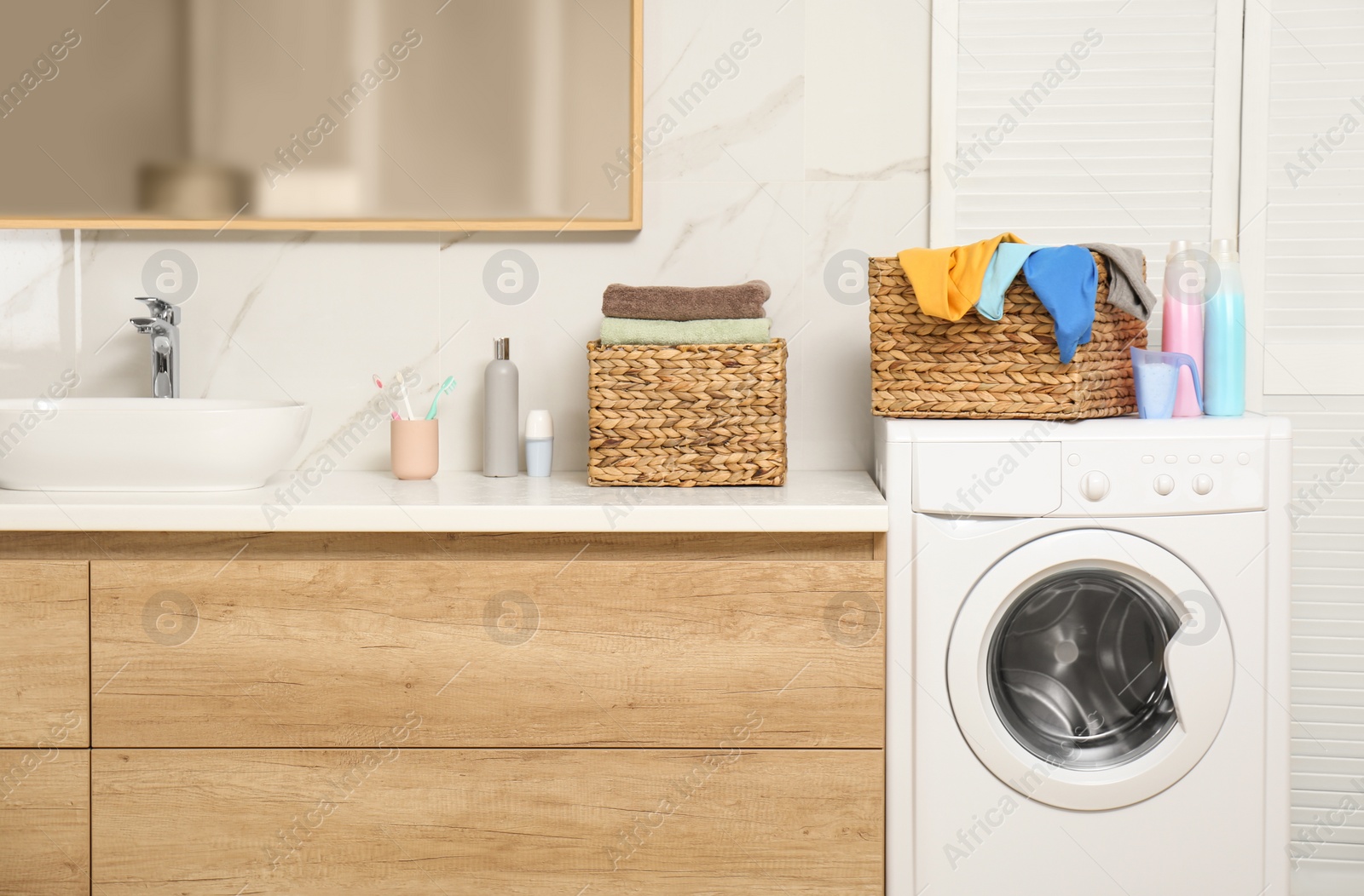 Photo of Wicker basket with laundry and detergents on washing machine in bathroom