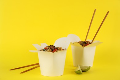 Boxes of wok noodles with vegetables, meat and chopsticks on yellow background