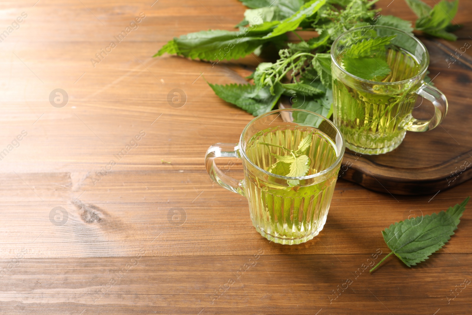 Photo of Aromatic nettle tea and green leaves on wooden table, space for text