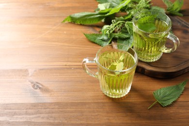 Photo of Aromatic nettle tea and green leaves on wooden table, space for text