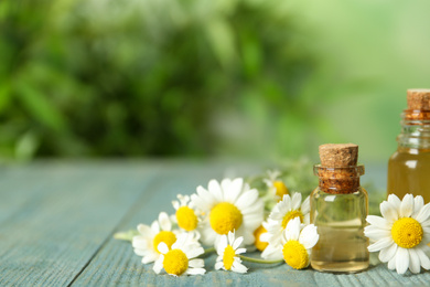 Photo of Bottles of essential oil and chamomiles on blue wooden table. Space for text