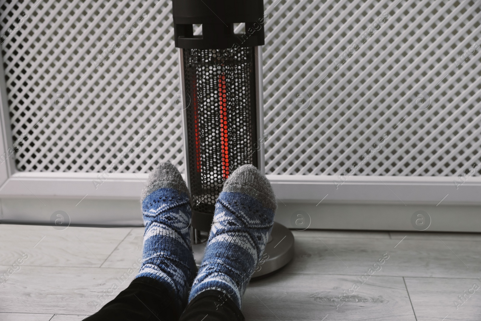 Photo of Man warming feet near modern heater indoors, closeup