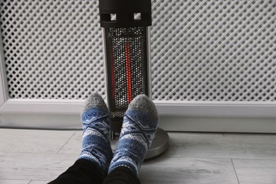 Photo of Man warming feet near modern heater indoors, closeup