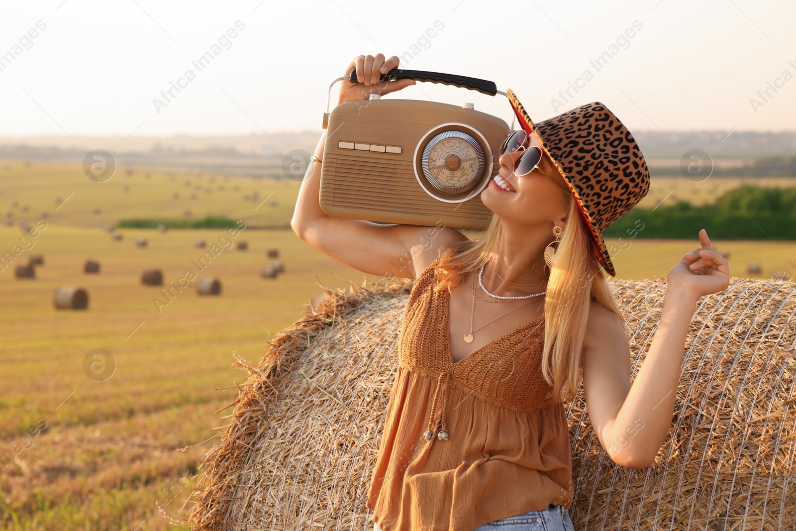 Photo of Happy hippie woman with radio receiver near hay bale in field, space for text