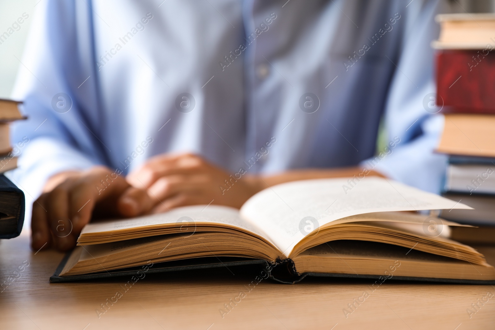 Photo of Woman reading hardcover book at wooden table indoors, closeup