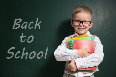 Image of Cute little child wearing glasses near chalkboard with phrase BACK TO SCHOOL