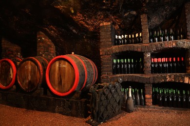Bene, Ukraine - June 23, 2023: Many wooden barrels and bottles with different alcohol drinks in cellar