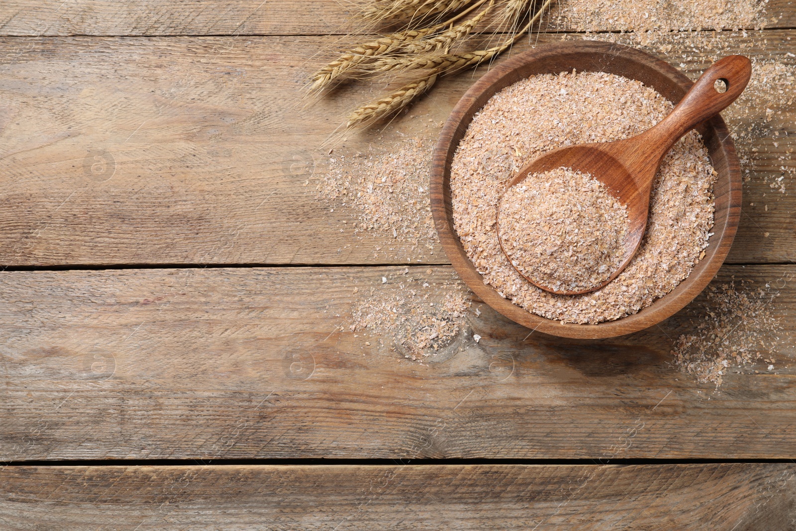 Photo of Wheat bran and spoon in bowl on wooden table, flat lay. Space for text