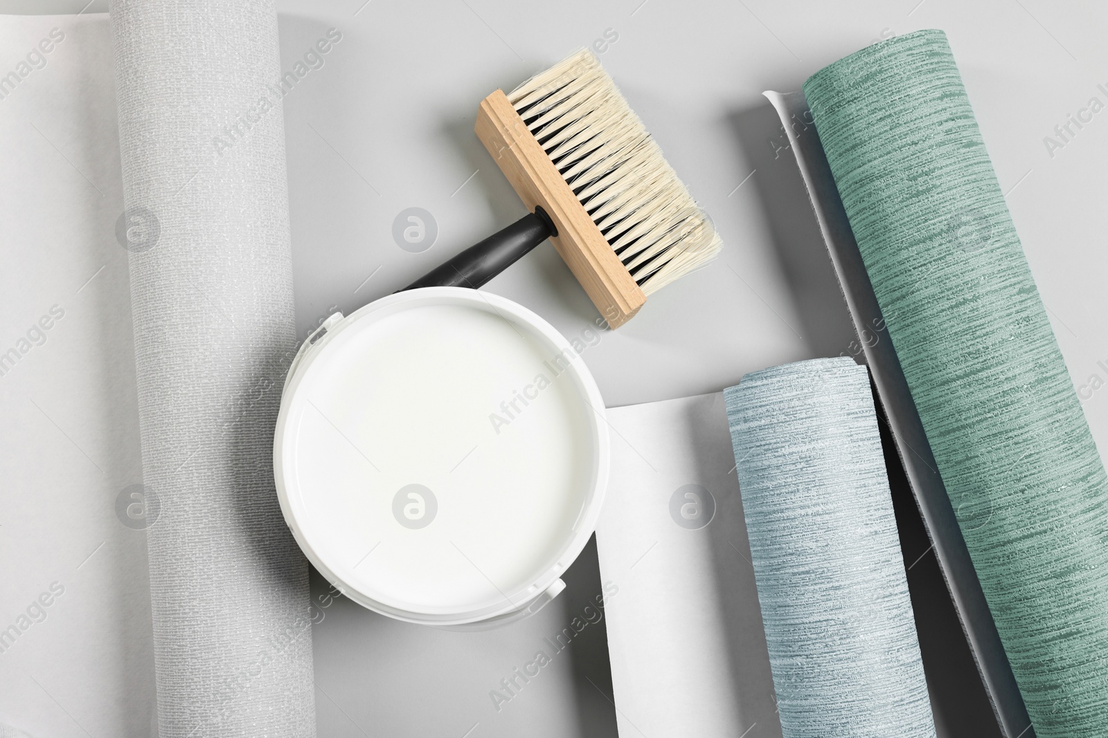 Image of Wallpaper rolls, brush and bucket of glue on light grey background, flat lay