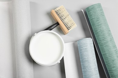 Wallpaper rolls, brush and bucket of glue on light grey background, flat lay