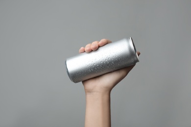 Photo of Woman holding aluminum can with beverage on grey background, closeup. Space for design