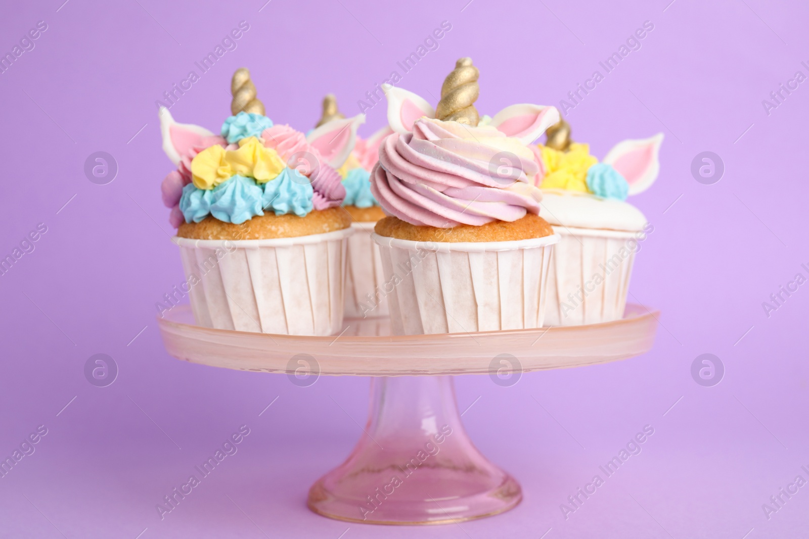 Photo of Cute sweet unicorn cupcakes on dessert stand against violet background