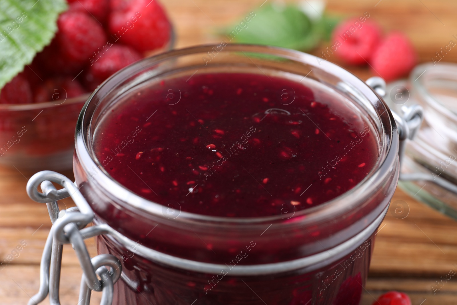 Photo of Glass jar of delicious raspberry jam on table, closeup