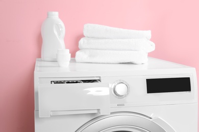 Photo of Bottle with detergent and clean towels on washing machine in laundry room
