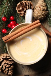 Photo of Tasty eggnog, cinnamon sticks and fir branches on wooden table, flat kay