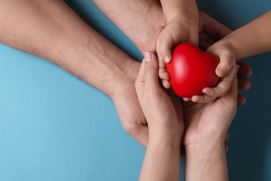 Photo of Parents and child holding red decorative heart on light blue background, top view. Space for text