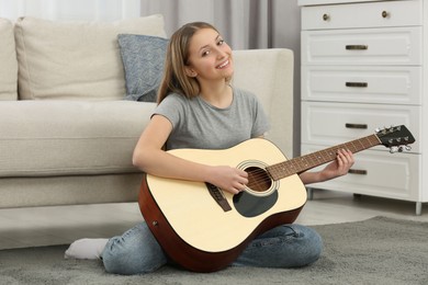 Photo of Teenage girl playing acoustic guitar near sofa in room