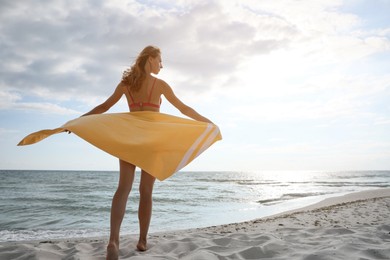 Beautiful woman with beach towel near seashore, back view